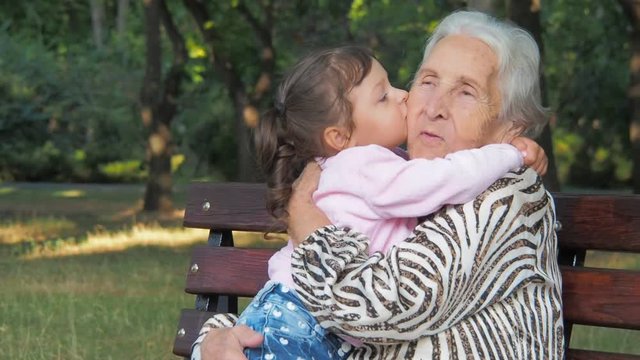 A child kisses an elderly woman. A little girl hugs her grandmother.