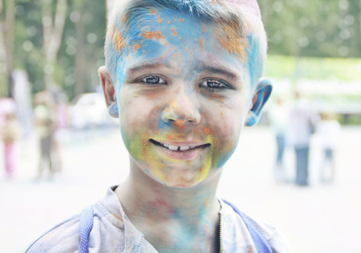 Portrait of a smiling teenage boy with multi-colored face at the festival in the park