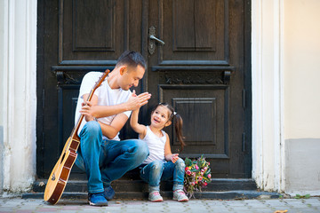 Dad Uchik daughter playing the guitar sitting on the doorstep of the house.