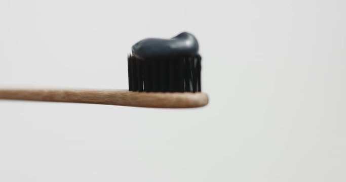 Black toothpaste on toothbrush with black bristles and wooden handle isolated on colorful backgrounds