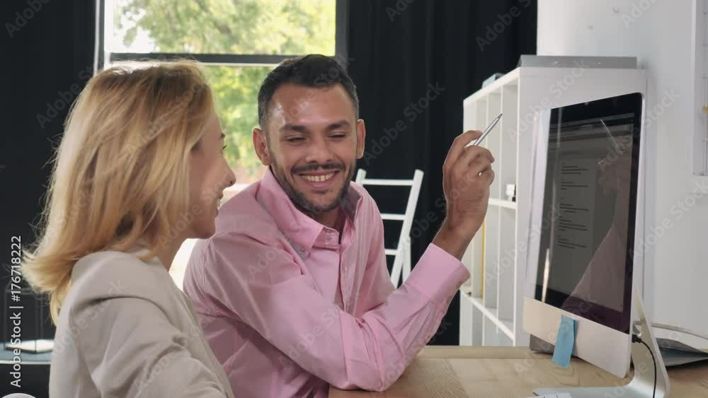 Poster Office workers sitting at the desk with computer. Handsome man pointing on monitor discussing with business woman some information or project. Friendly happy people working in office