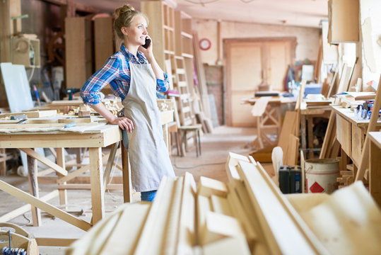 Portrait of modern young woman speaking by phone in carpenting shop taking break from work, copy space