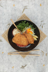 Top view of Fried tempura whiting fish or asohos with home made tomato sauce served with sliced cabbage, lettuce, lemon and egg salad in round black plate with chopstick on makisu (meal mat).