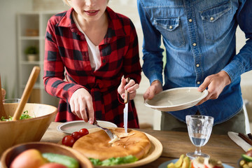 Mid section portrait of modern young couple  standing at festive dinner table  cutting food  during family celebration - Powered by Adobe