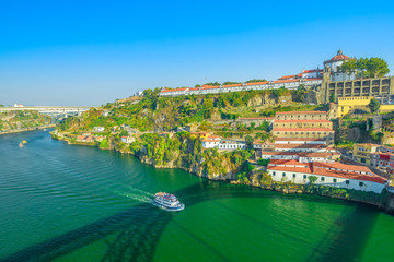 Fototapeta premium Aerial view of tourist boat in Douro River and Unesco Monastery of Serra do Pilar from Dom Luis I Bridge in Vila Nova de Gaia, Porto, Portugal. Oporto urban scenic landscape in the blue sky.