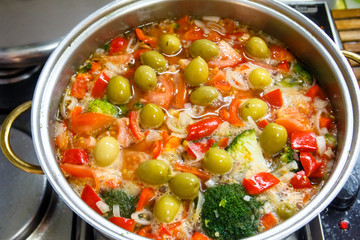 Vegetable soup of tomatoes, peppers, broccoli and olives cooked in a saucepan.