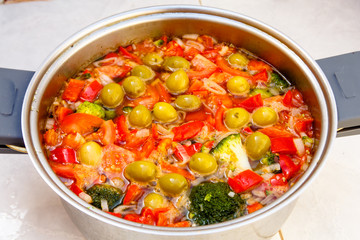 Vegetable soup of tomatoes, peppers, broccoli and olives cooked in a saucepan.