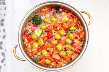 Vegetable soup of tomatoes, peppers, broccoli and olives cooked in a saucepan.