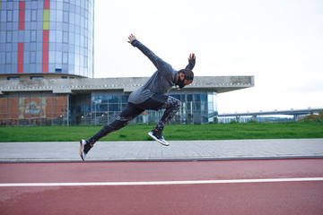 Respiratory сonditioning for exercise. Side view of Afro American athlete training at stadium, doing high jumps, using training mask to improve strenght and power during cardio workout session