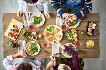 Top view of four people eating delicious food at festive dinner table  in cafe or restaurant celebrating holiday