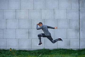 Sideview summer portrait of strong determined young dark-skinned sportsman exercising outdoors, jumping high against brick wall background with copy space for your information. Freeze action shot