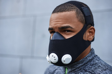 Breathing technologies for fitness and sport. Portrait of young muscular Afro American sportsman wearing respiratory resistance device to strengthen breathing muscles and improve breathing mechanics