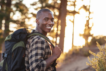 Smiling young African man hiking along a trail at dusk
