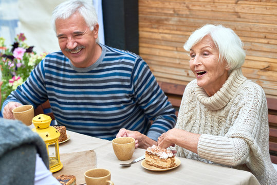 Portrait of happy senior couple laughing enjoying dinner with friends and family drinking tea with cakes on outdoor terrace