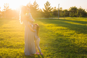 Beautiful woman with daughter and baby son on green grass field. Mother with two little children hugging outdoors. Happy family concept