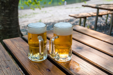 Pair of freshly filled beer glasses, over a table in front of lake