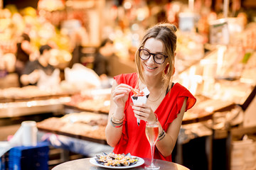 Young woman in red dress eating jamon traditional spanish dry-cured ham sitting at the Barcelona...