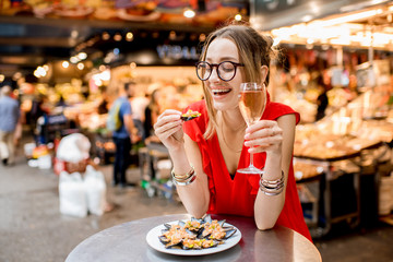 Young woman in red dress having lunch with mussels and rose wine sitting at the food market