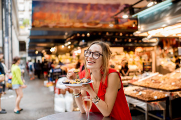 Young woman in red dress having lunch with mussels and rose wine sitting at the food market