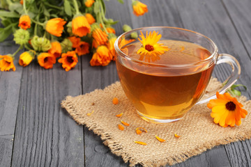 Calendula tea with fresh flowers on black wooden background