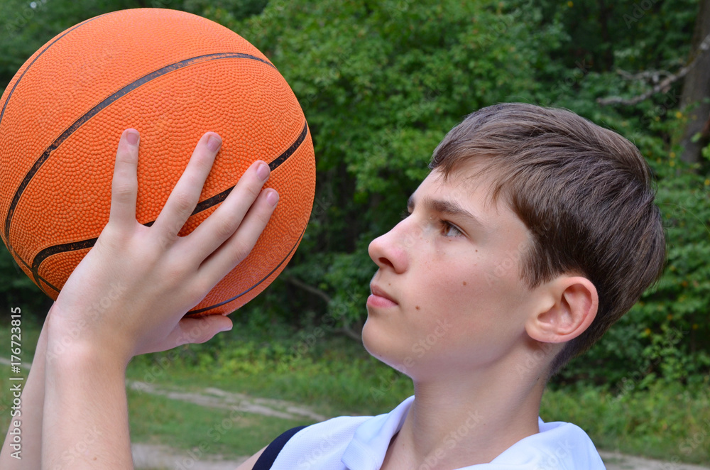 Wall mural Teenager boy in a white shirt with a ball for basketball 
