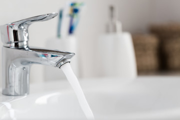 Water tap with turned on water in modern bathroom