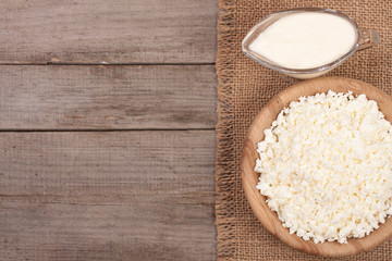 Cottage cheese in a wooden bowl with sour cream on old wooden background with copy space for your text. Top view