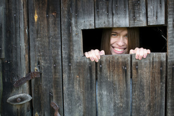 Young woman smiling looking out the window in a wooden shed.