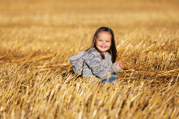 Naklejka na ściany i meble Happy 2 year old girl walking in a summer harvested field
