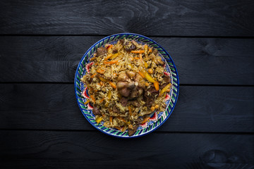 Pilaf on plate with oriental ornament on a wooden background. Central-Asian cuisine - Plov. Top view
