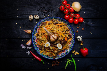 Pilaf and ingredients on plate with oriental ornament on a dark wooden background. Central-Asian...