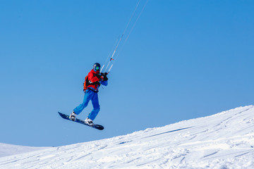 Naklejka na ściany i meble Snowboarder with a kite on fresh snow in the winter in the tundra of Russia against a clear blue sky. Teriberka, Kola Peninsula, Russia. Concept of winter sports snowkite.