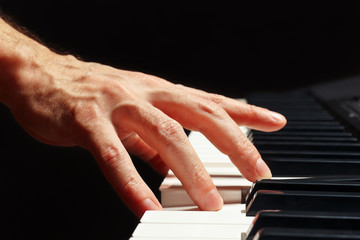 Hand of pianist play the keys of the electronic organ on a black background close up