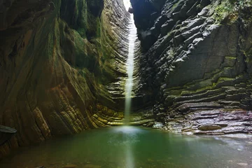Fotobehang Beautiful grotto with a pouring beautiful waterfall © Boris Bulychev