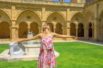 Naklejka premium Freedom woman with open arms at old Coimbra Cathedral cloister. Se Velha de Coimbra is one of most important romanesque buildings in Portugal. Female tourist enjoying in university town of Coimbra.