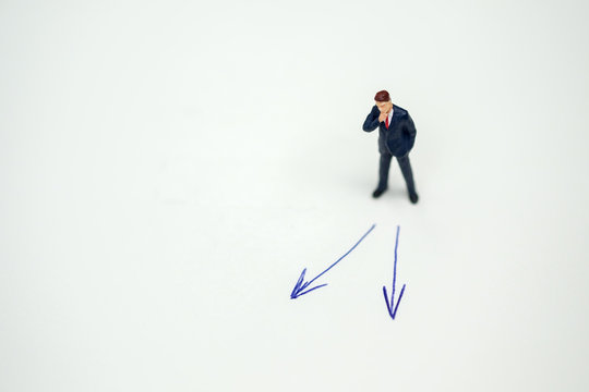 Business direction, decision and planning concept. Businessman miniature figure standing and thinking on paper with 2 arrow sign.