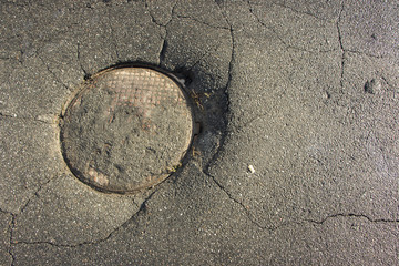 Large pothole in asphalt and circular manhole cover of sewage well in road,
