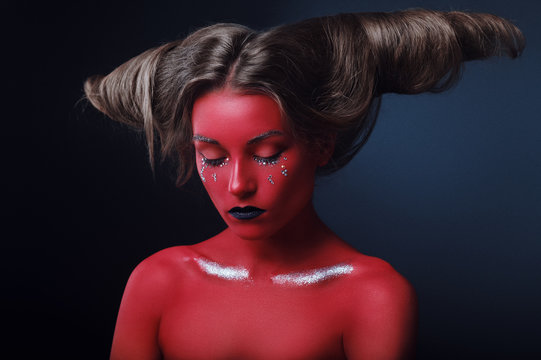 Portrait of a girl in a high fashion, beauty style with red skin, black lips make up at dark background. Devil makeup fashion art design. Halloween holiday concept