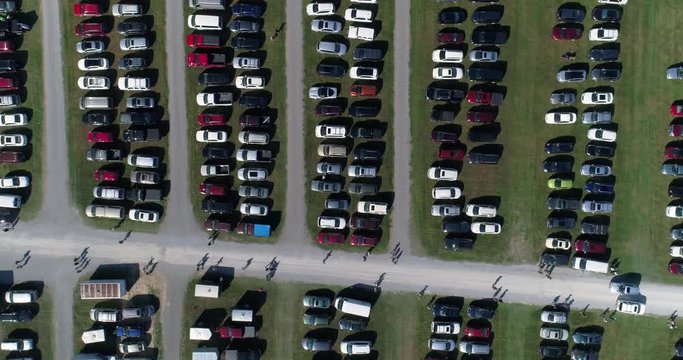 A high view looking straight down on cars and people in a parking lot in an Ohio field outside of a fair.  	