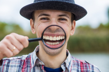 Fototapeta premium A cheerful young man with a funny face in a hat holds a magnifying glass. Let's celebrate! 