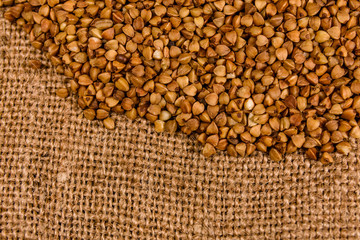 Fototapeta premium Pile of the raw buckwheat on sackcloth. Top view