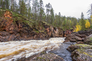 Red cliff, stone wall, forest, waterfall and wild river view in autumn. Fall colors - ruska time in Kiutaköngäs. One part of Karhunkierros Trail. Oulanka National Park, north Finland, Lapland, Europe