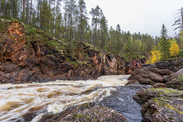 Red cliff, stone wall, forest, waterfall and wild river view in autumn. Fall colors - ruska time in Kiutaköngäs. One part of Karhunkierros Trail. Oulanka National Park, north Finland, Lapland, Europe