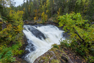 Fototapeta na wymiar Cliff, stone wall, forest, waterfall and wild river view in autumn. Fall colors - ruska time in Myllykoski. One part of Karhunkierros Trail. Oulanka National Park in north Finland. Lapland, Europe