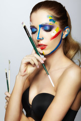 Young female painter with  paint brush in hand  and  acrylic paint on face