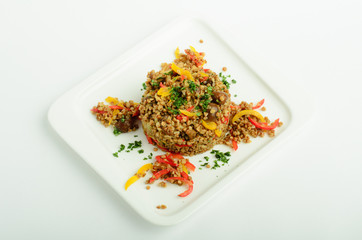 Buckwheat with bell pepper and mushrooms on a plate isolated on white background