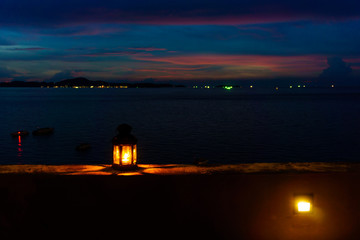 The light or lantern is shining in the dark and placed on the edge of the mortar with sea and twilight sky at night as background.