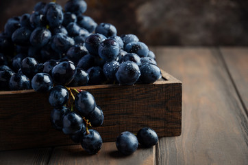 Fresh Black Grapes in Dark Wooden Tray on Wooden Table Selective focus Copy Space