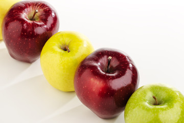 Multicolored apples in a row on a white table