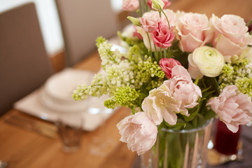 Blumenstrauß auf einem classisch gedekten holztisch mit weißen tellern in großen offenem Raum